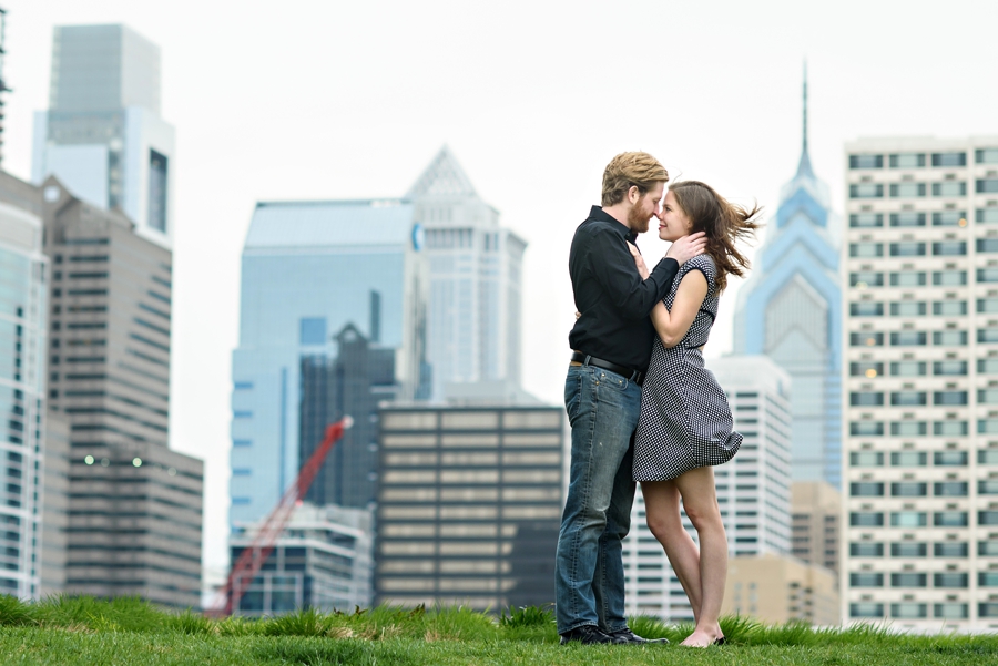 A couple embrace in front of the philadelphia skyline while the wind blows through their hair during their engagement session.